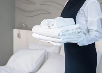 servicio-habitacion-hotel-haciendo-habitacion-mujer-joven-camarera-sosteniendo-pila-toallas-bano-blancas-dobladas-pie-junto-cama-habitacion-invitados_63313-1772 Ay7AhFOGdpIArsgDB0euEOYAAAAASUVORK5CYII=